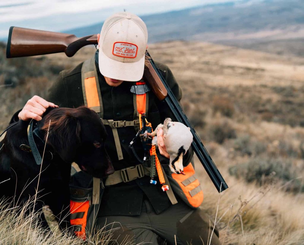 A hunter with a dog and chukar after a successful hunt.